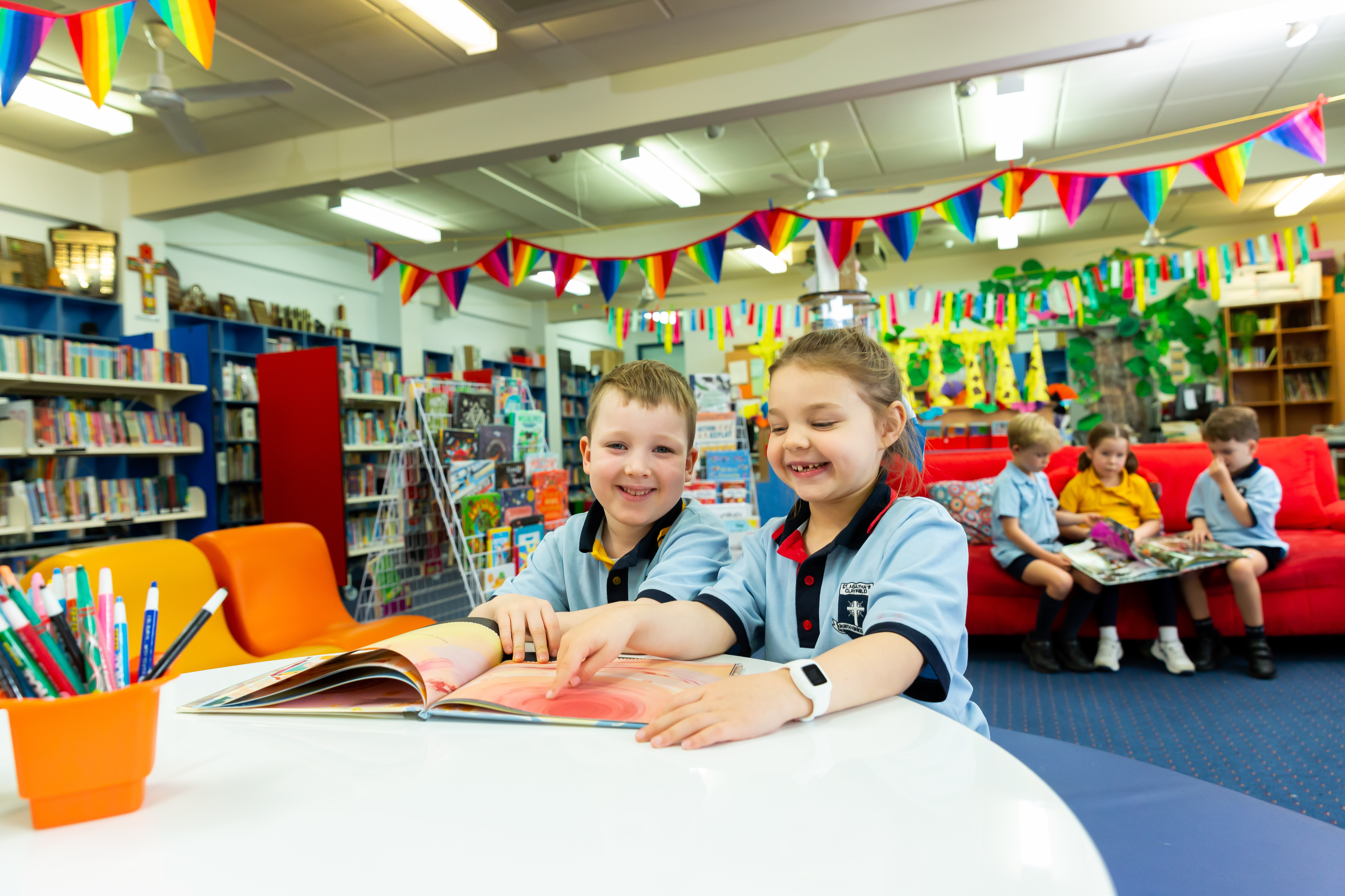 Students reading a book together at a table in the school library with colourful bunting and bookshelves in the background