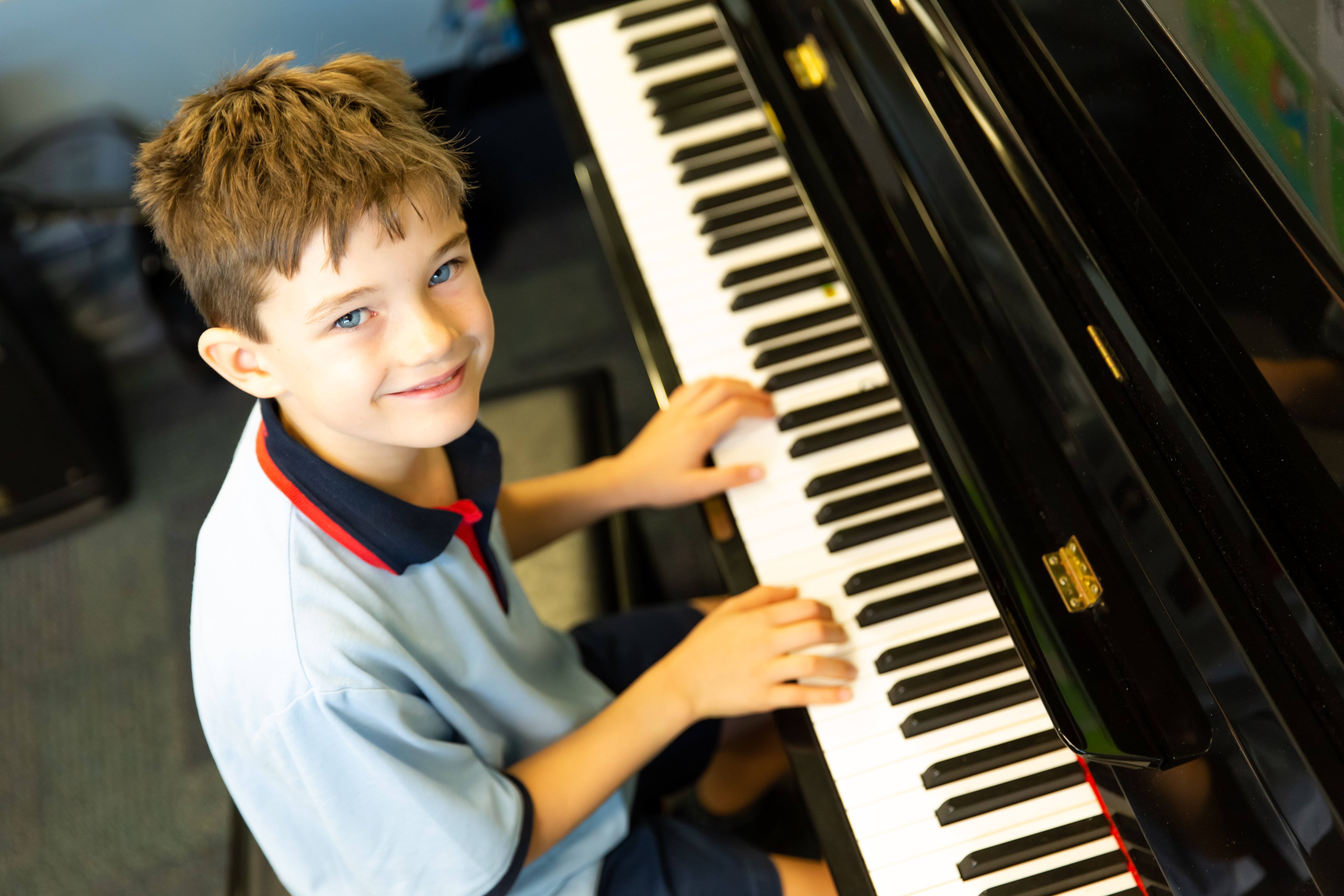 Student seated at a piano playing the keys in a school music space