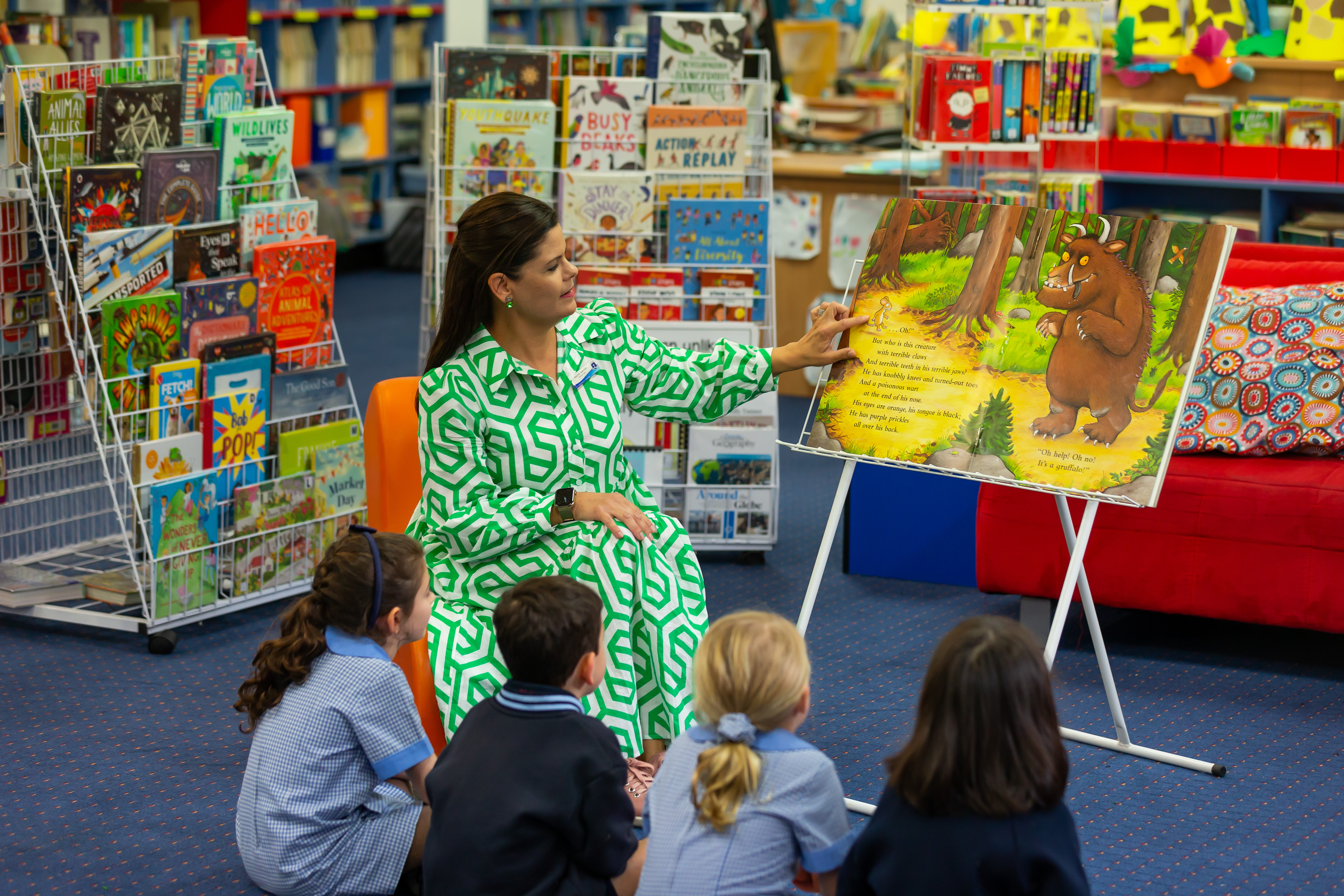 Teacher reading a picture book to a small group of students seated on the floor in the school library
