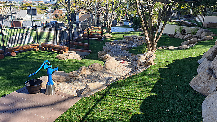 Nature play space with rocks, grass and a hand water pump