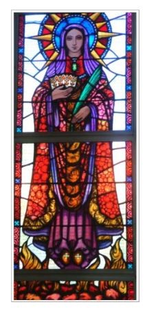 Stained glass window depicting a crowned female saint holding a palm branch, dressed in flowing robes with rich red, purple and gold tones, framed by decorative patterned panels