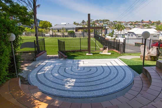 Circular stone prayer labyrinth with a wooden cross overlooking school grounds