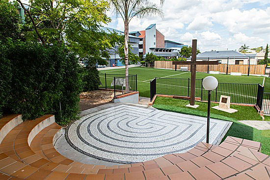 Outdoor prayer labyrinth with a cross and seating area on school grounds