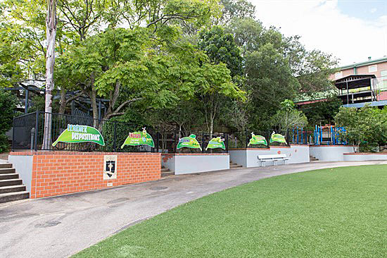 School playground and seating area with banners and play equipment beside a grass field