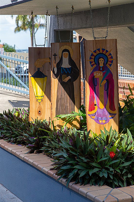 Outdoor religious artwork showing painted wooden panels with saints and lantern imagery