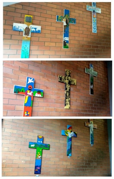 A series of colourful student‑designed crosses displayed on an indoor brick wall