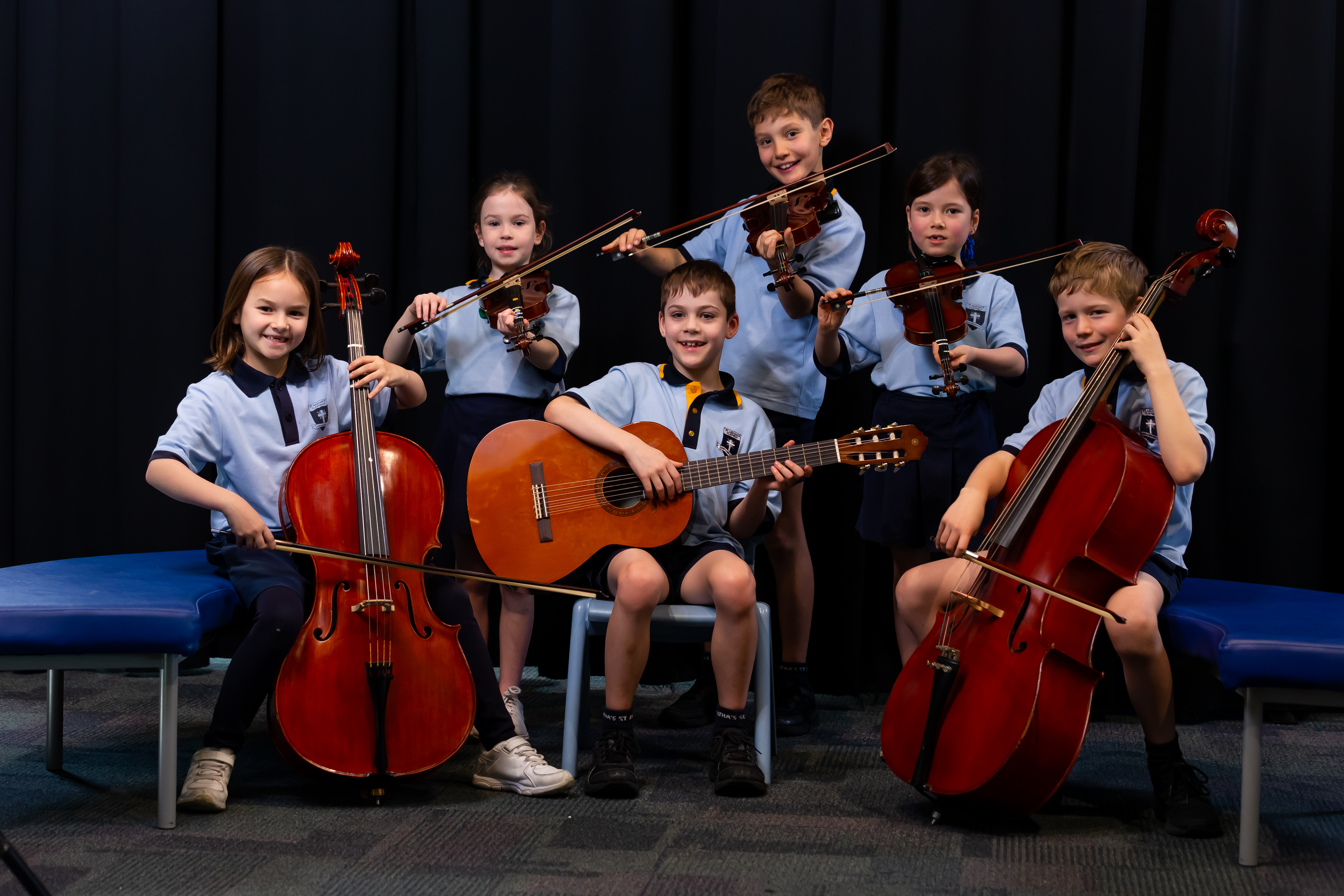 Students seated together holding string instruments and a guitar during a school music ensemble activity