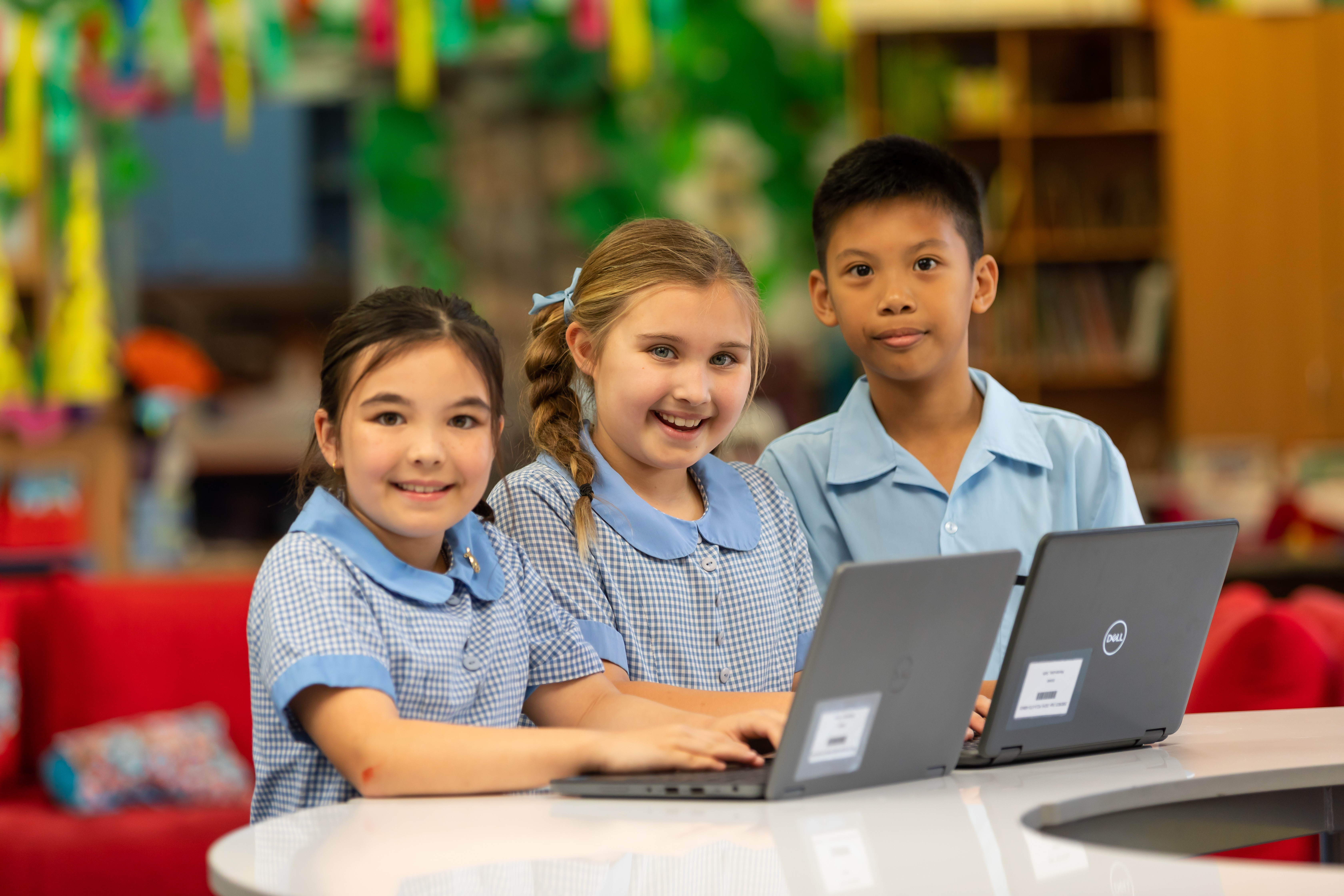 Three students using laptops together at a table in a school learning space