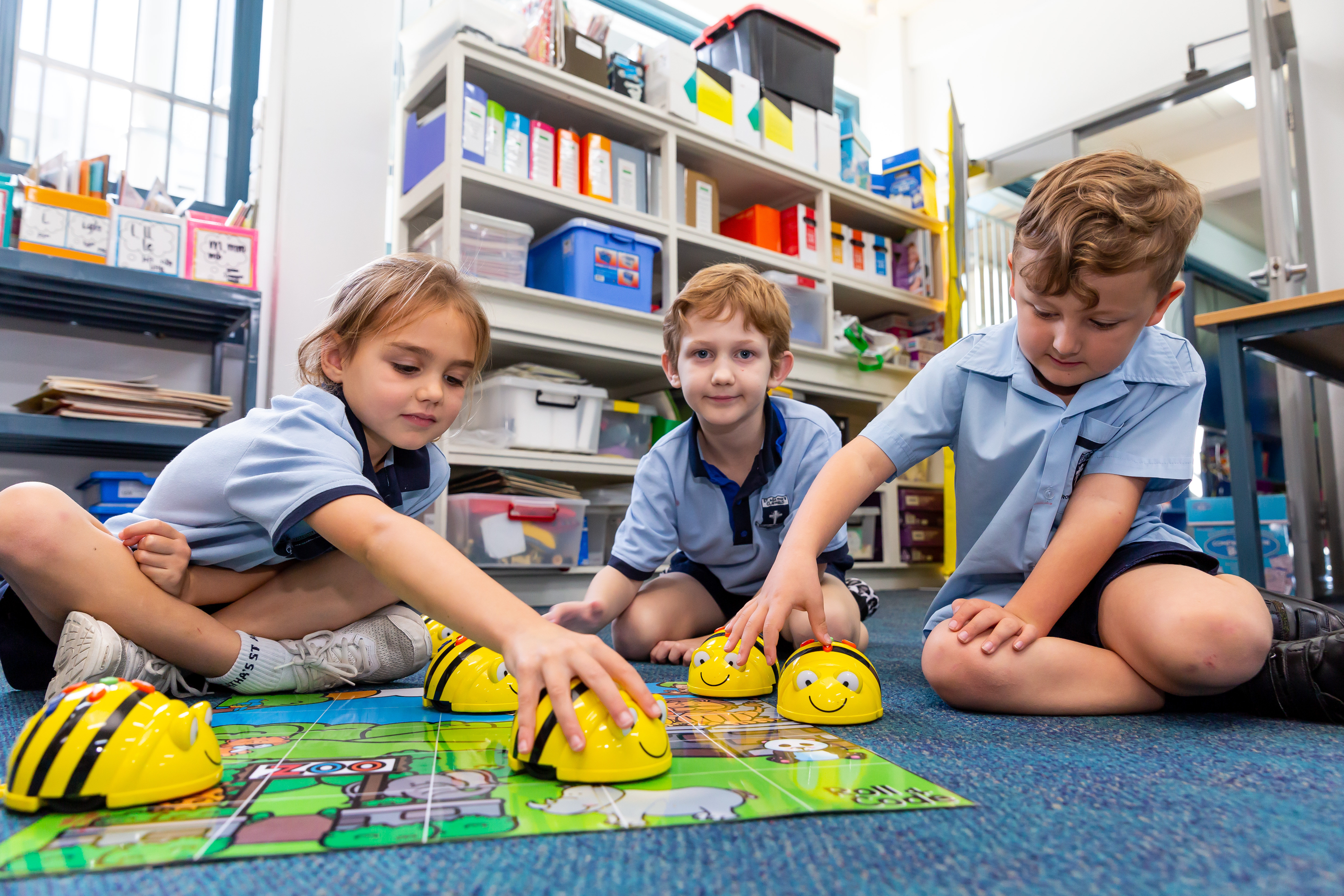 Three students using bee robots on a floor mat during a hands-on coding activity