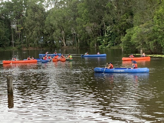 Students canoeing together on a calm lake during a school outdoor education activity