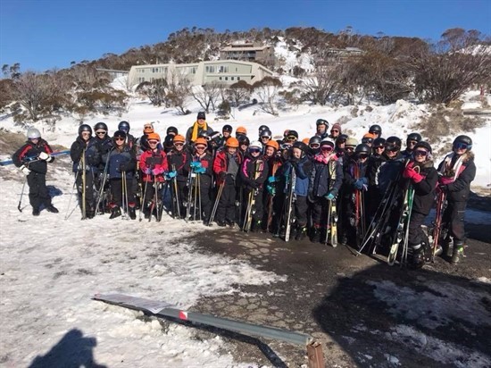 Large group of students in ski gear standing together on a snowy slope during a school ski trip