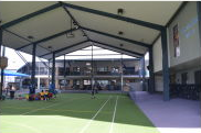 Covered multi‑purpose sports court with marked playing areas and school buildings in the background