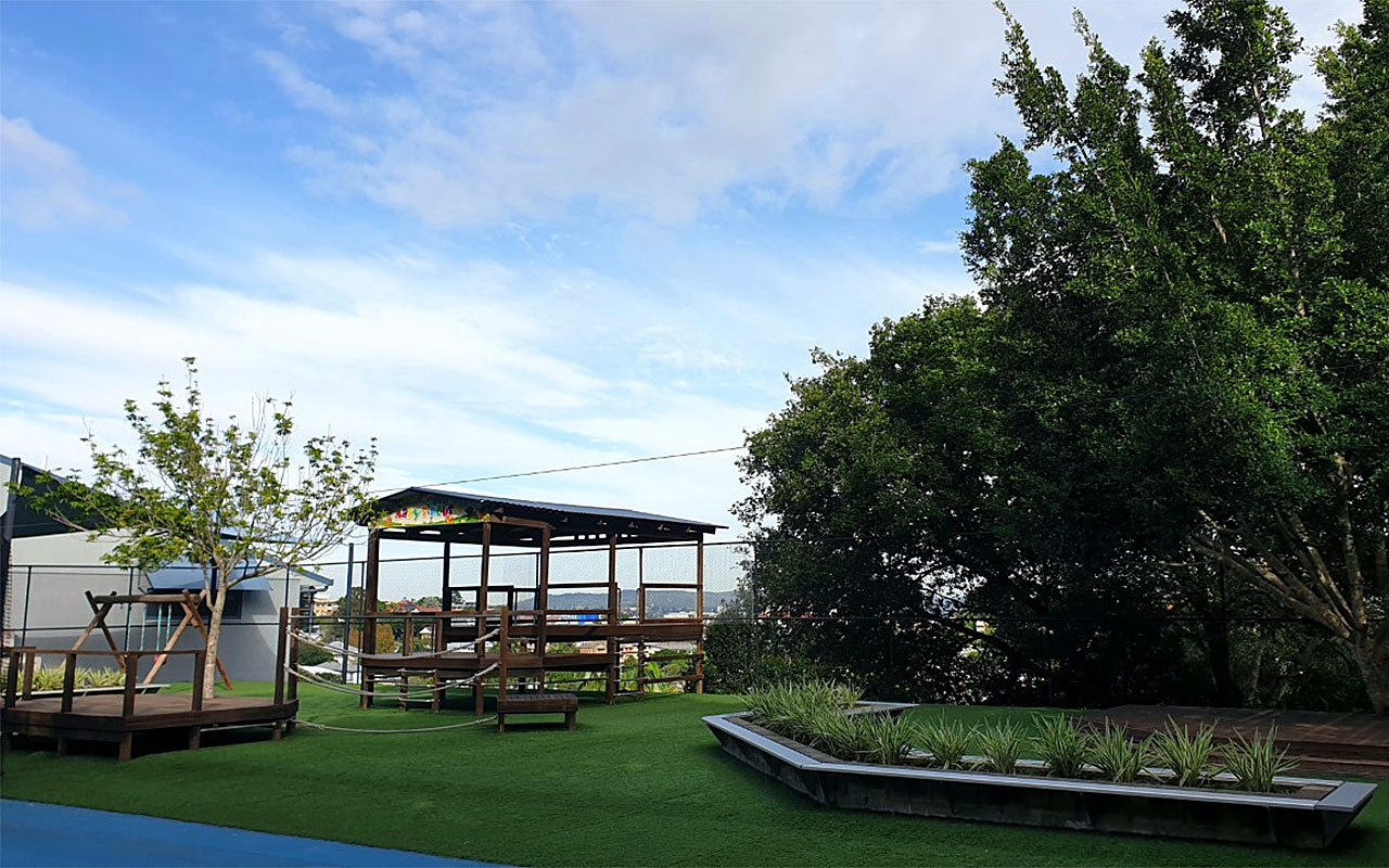 Outdoor learning area with grass, seating, trees and a shaded wooden shelter
