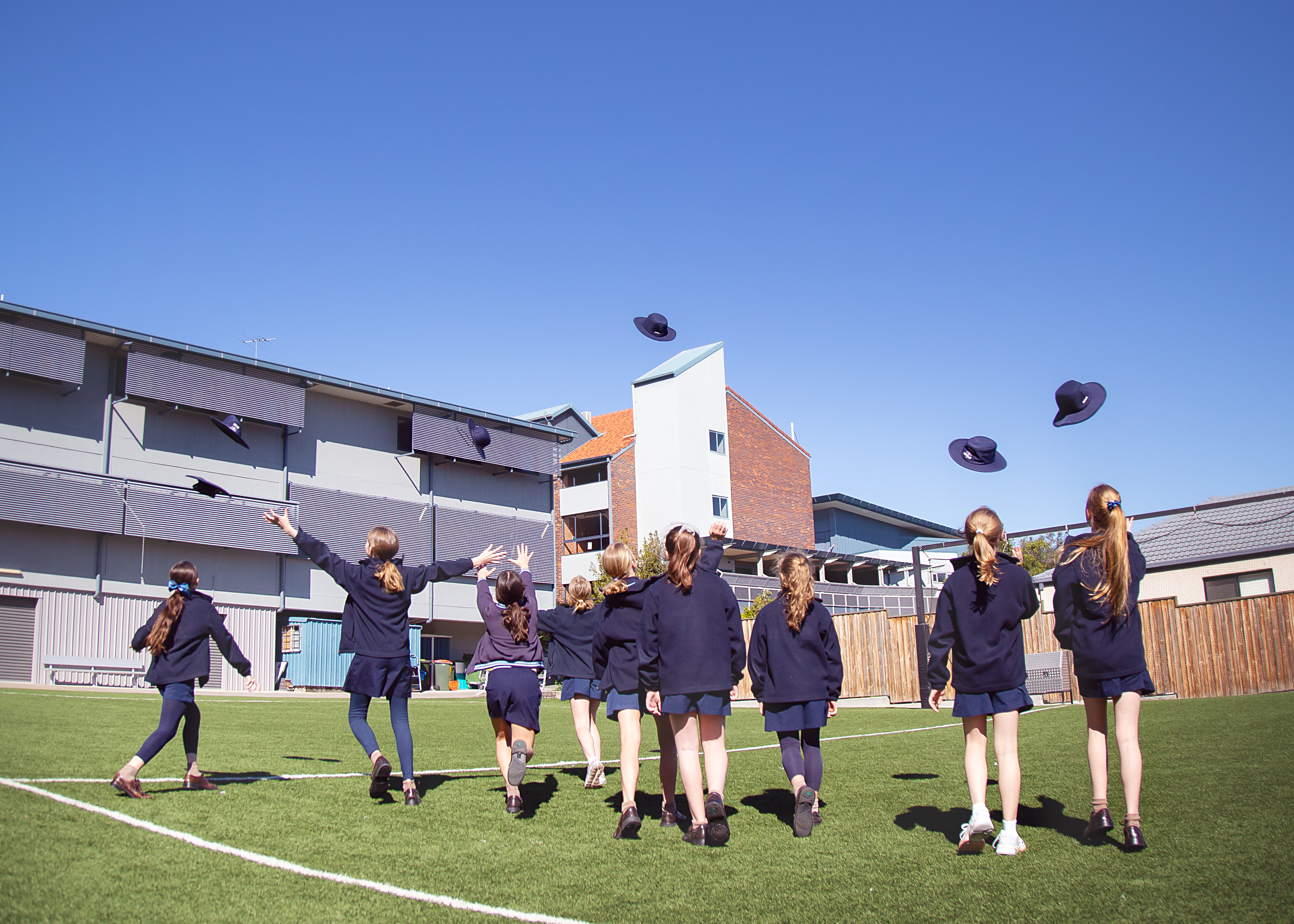 Students outdoors on a school oval throwing their hats into the air in celebration near school buildings