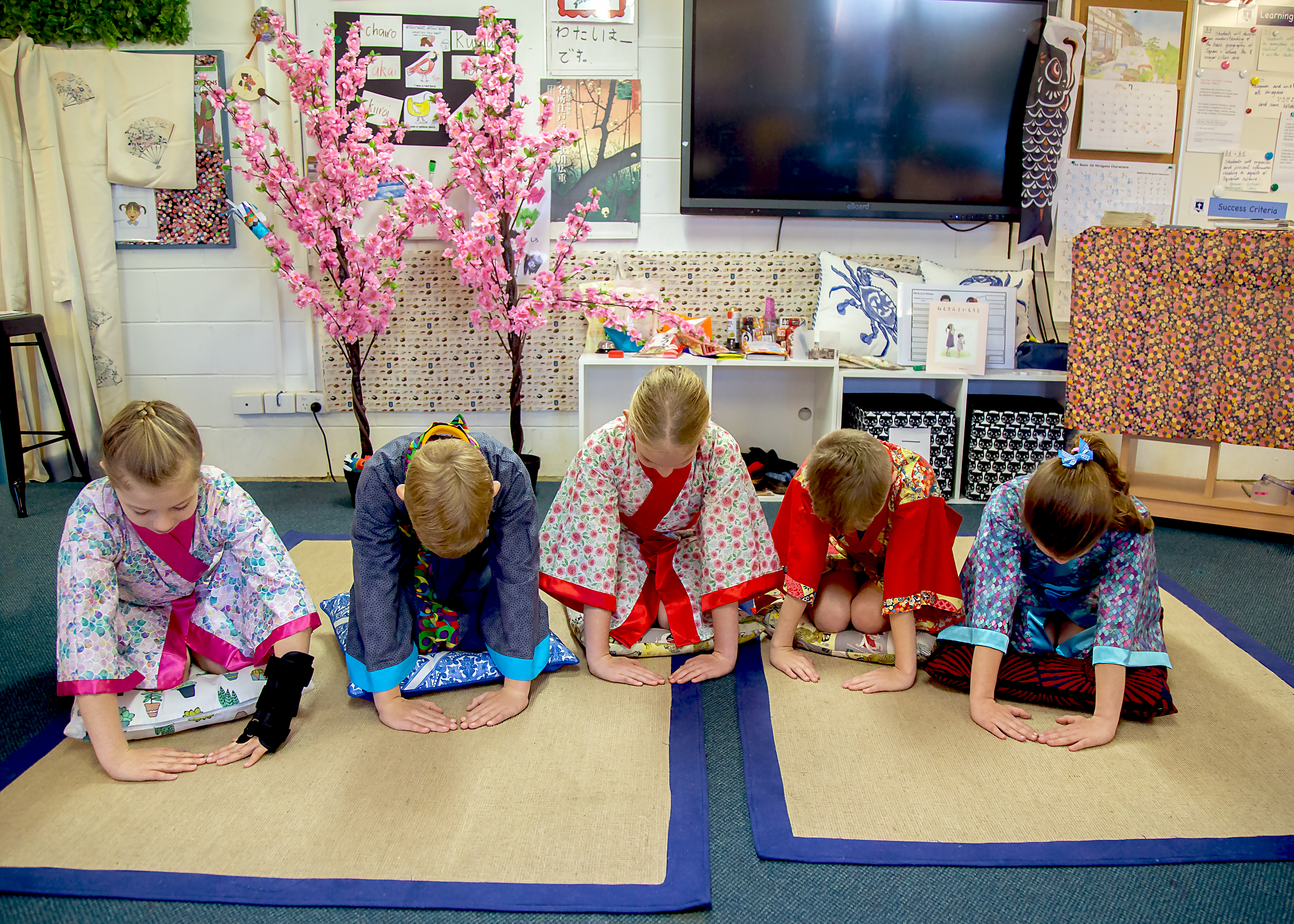 Students wearing traditional clothing bowing together during a cultural learning activity in the classroom