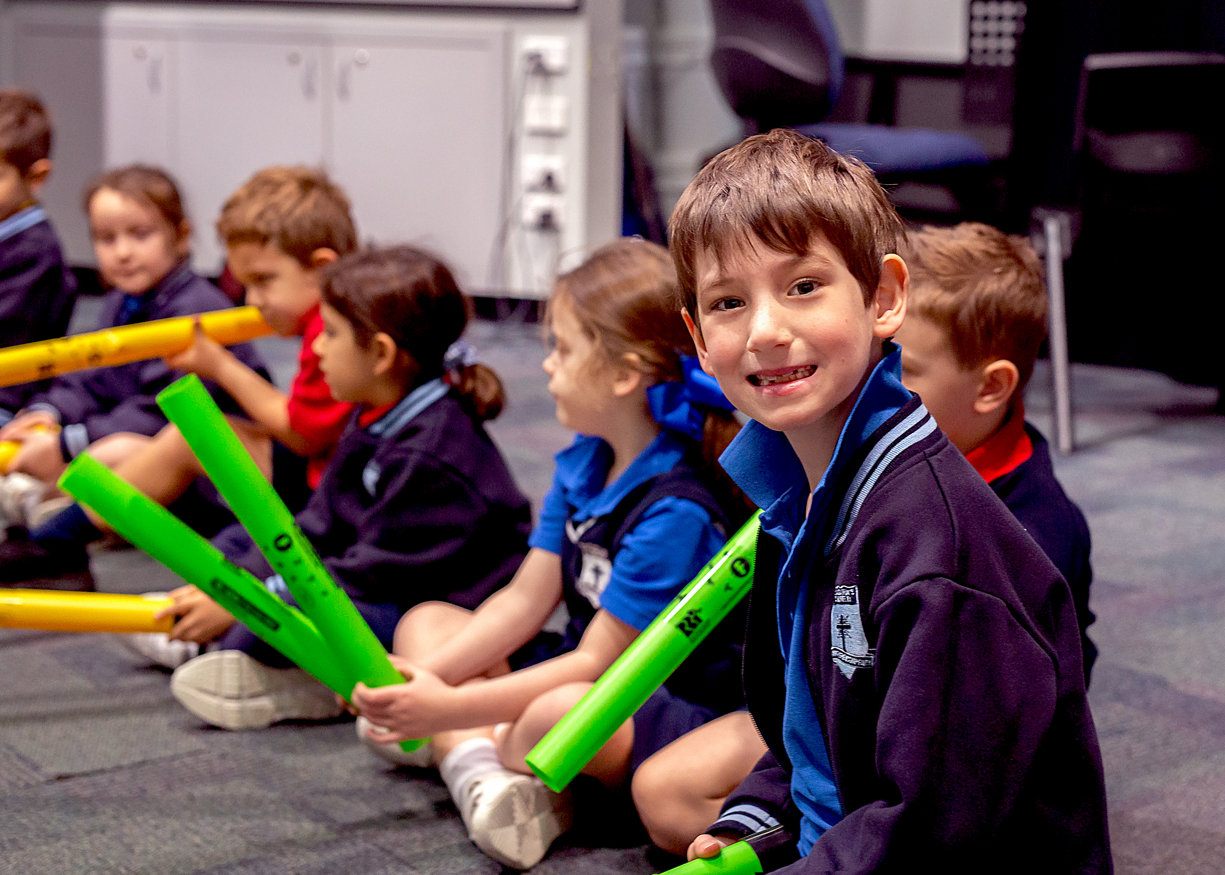 Students seated indoors holding rhythm sticks during a music activity